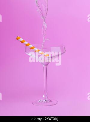 Verre à martini clair avec paille de papier orange et blanc rempli d'eau sur fond rose Banque D'Images