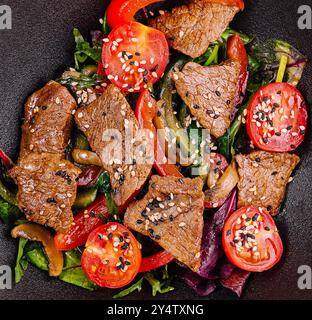 Salade avec tranches de bœuf grillées, légumes frais, champignons et graines de sésame sur une assiette noire Banque D'Images