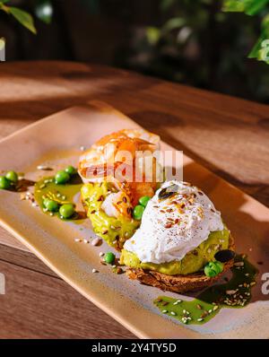 Deux tranches de pain grillé à l'avocat, l'une avec des crevettes et l'autre avec un œuf poché, sont assis sur une assiette avec une garniture verte Banque D'Images