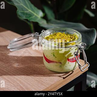 Dessert à la pistache avec gelée de fruits rouges saupoudrée de pistaches écrasées dans un bocal en verre avec couvercle ouvert Banque D'Images