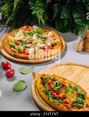 Pizza salade César et pide turque avec tomates séchées au soleil et épinards couchés sur des planches de bois sur une table grise Banque D'Images