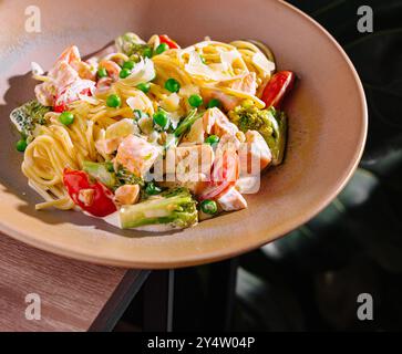 Plat de pâtes au saumon avec pois verts, bouquets de brocoli, parmesan et sauce crémeuse servi dans un cadre de restaurant Banque D'Images