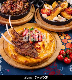 De délicieuses côtes d'agneau grillées servies sur du pain plat avec une salade de tomates fraîches et d'oignons sur une table de restaurant Banque D'Images