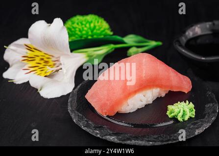 Sushi maguro nigiri fraîchement préparé servi sur une ardoise noire avec wasabi, sauce soja et fleurs Banque D'Images