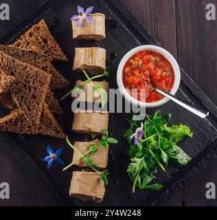Pâté de foie de poulet décoré de fleurs et de microgreens est servi sur une assiette en pierre noire avec des toasts de pain de seigle et de la sauce Banque D'Images