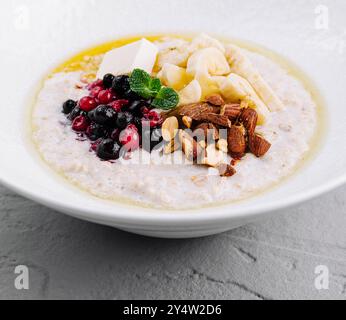 La bouillie d'avoine est garnie de baies, d'amandes, de tranches de banane et de menthe dans un bol blanc pour un petit déjeuner sain Banque D'Images