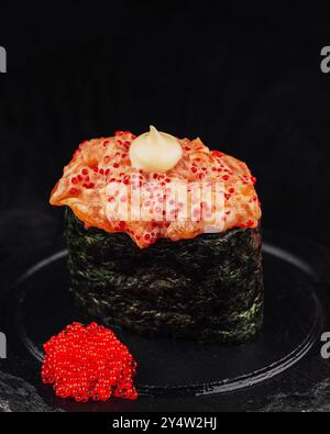 Sushi Gunkan maki nappé de saumon épicé et de caviar tobiko rouge, servi dans une assiette noire Banque D'Images