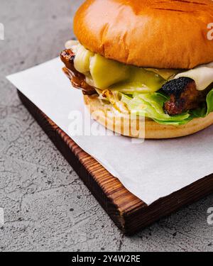 Hamburger avec escalope de poulet, fromage fondu et feuilles de laitue couché sur une planche de bois et du papier parchemin blanc Banque D'Images