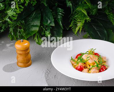 Tagliatelles aux crevettes et tomates décorées de roquette servies sur assiette blanche près du moulin à poivre sur fond gris texturé Banque D'Images