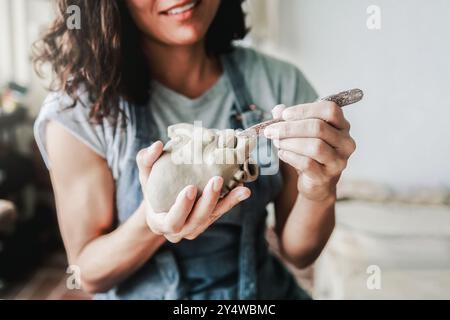 Poterie d'art, travail d'artiste avec sculpture en céramique à l'atelier d'argile. Vue rognée, femme sculptant la forme d'un coeur. Petites entreprises et artisanat fait à la main Banque D'Images