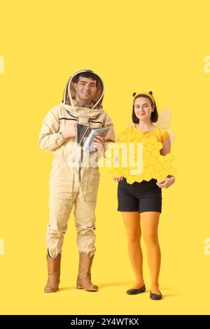 Apiculteur masculin avec fumeur et femme en costume d'abeille sur fond jaune Banque D'Images