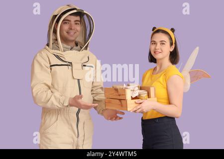 Apiculteur masculin avec miel et femme en costume d'abeille sur fond lilas Banque D'Images