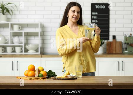 Belle jeune femme avec pichet d'eau infusée au citron dans la cuisine Banque D'Images