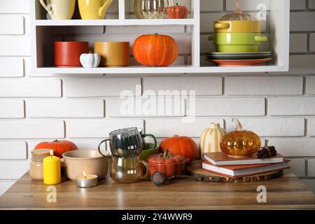 Vaisselle avec citrouilles, livres et bougies allumées sur le comptoir près du mur de briques blanches Banque D'Images