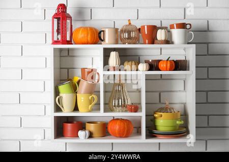 Étagères avec vaisselle et citrouilles sur mur de briques blanches Banque D'Images