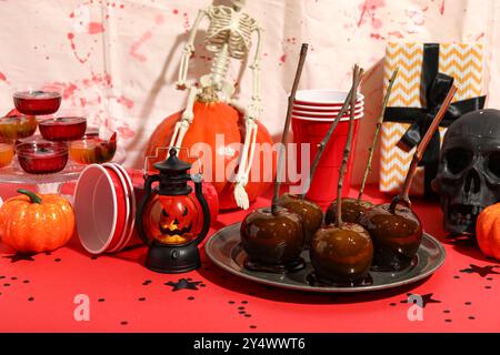 Friandises sucrées, tasses en plastique et décorations pour la fête d'Halloween sur la table rouge Banque D'Images