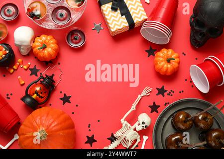 Cadre fait de friandises sucrées, de tasses en plastique et de décorations pour la fête d'Halloween sur fond rouge Banque D'Images