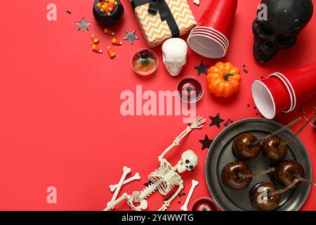 Composition avec des friandises sucrées, des tasses en plastique et des décorations pour la fête d'Halloween sur fond rouge Banque D'Images