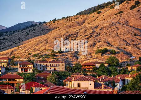 Le village d'Agios Germanos en Grèce, niché au pied de collines arides, illuminé par la lumière chaude du coucher de soleil, avec des maisons traditionnelles en pierre et Banque D'Images