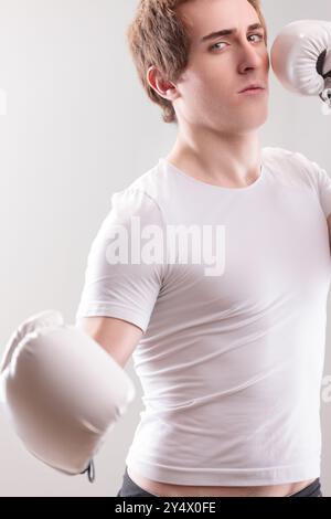 Jeune homme portant une chemise blanche et des gants de boxe maintient une position concentrée, prêt à défendre ou frapper au besoin Banque D'Images