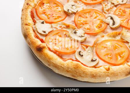 Gros plan d'une pizza fraîchement cuite garnie de tranches de tomates et de champignons sur fond blanc. Banque D'Images