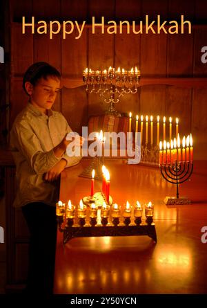 Un jeune garçon tient une bougie allumée et allume la menorah Hanukkah pendant les huit jours de la fête juive des Lumières. Banque D'Images