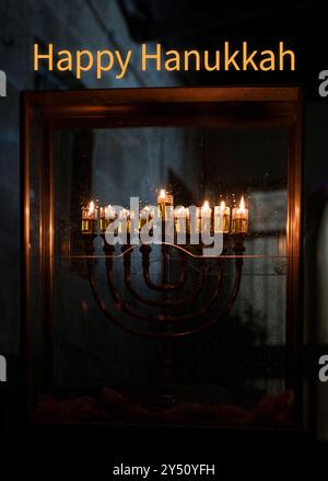 Hanukkah salutation en anglais avec une menorah devant une maison à Jérusalem, Israël, avec huit bougies à huile brûlant la huitième nuit du holi juif Banque D'Images