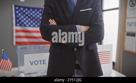 Homme hispanique avec les bras croisés se tient confiant dans un centre de vote américain, affichant la démocratie et les thèmes gouvernementaux. Banque D'Images