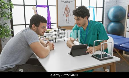 Un physiothérapeute consulte un patient masculin dans une salle de thérapie moderne, discutant de la réadaptation sur un comprimé. Banque D'Images