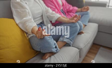 Deux femmes détendues assises sur un canapé de salon méditant ensemble à l'intérieur, mettant l'accent sur l'amitié, le calme et l'atmosphère chaleureuse d'une maison. Banque D'Images