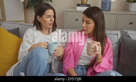 Deux femmes apprécient le café ensemble dans un salon confortable, s'engageant dans une conversation sur un canapé confortable. Banque D'Images