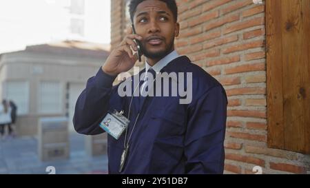 Homme afro-américain en tenue professionnelle parlant au téléphone par la rue de la ville avec badge et cordon Banque D'Images