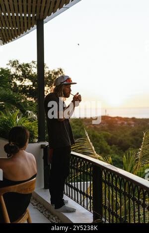 Un homme en vacances, fumant sur la terrasse au coucher du soleil. Banque D'Images