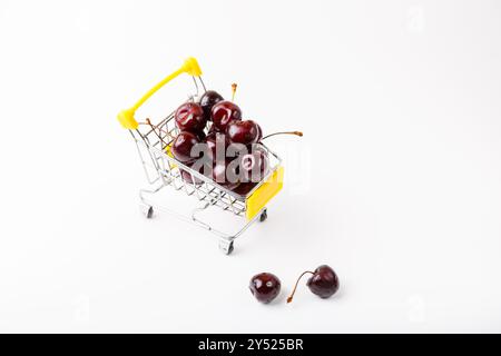 Cerise dans un petit chariot d'épicerie miniature pour un supermarché. Chariot à jouets avec baies sur fond blanc. Gros plan, espace de copie pour le texte, vue de dessus. Banque D'Images