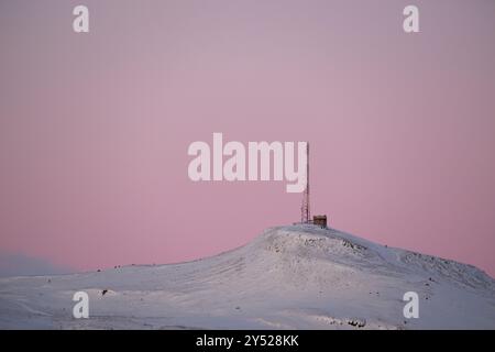 Mât d'antenne sur une colline enneigée pendant le coucher du soleil Banque D'Images