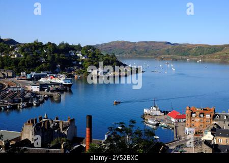 Oban, Écosse, Royaume-Uni. 20 septembre 2024. Glorieux temps chaud et ensoleillé à Oban et sur la côte ouest avec des vues sur la ville et le port, les conditions ensoleillées devraient continuer tout au long du week-end. Le ferry calédonien MacBrayne 'Isle of Mull' a accosté dans le terminal de ferry d'Oban, avec un petit bateau de pêche arrivant dans le port. Vue depuis la tour de McCaig. Crédit : Craig Brown/Alamy Live News Banque D'Images