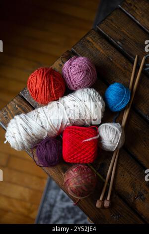 Boules de fil colorées et aiguilles à tricoter disposées sur une table en bois Banque D'Images