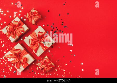 Plusieurs coffrets cadeaux avec des noeuds sur un fond rouge avec des lumières et des confettis en forme d'étoiles. Concept de vacances. Banque D'Images