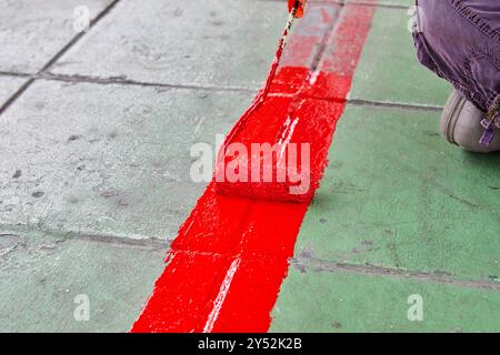 Travailleur utilisant le rouleau de peinture et peignant la couleur rouge sur le sentier Banque D'Images