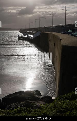 Jetée côtière sous un ciel nuageux, reflétant la lumière du soleil sur l'eau. Banque D'Images