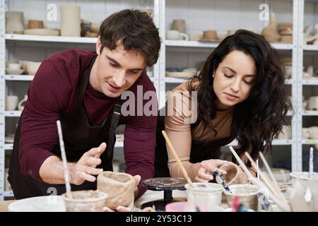 Un couple façonne joyeusement l'argile dans un atelier de poterie contemporaine. Banque D'Images