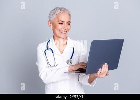 Photo de charmant médecin thérapeute joyeux qualifié spécialiste du centre de bien-être de travail isolé sur fond de couleur grise Banque D'Images