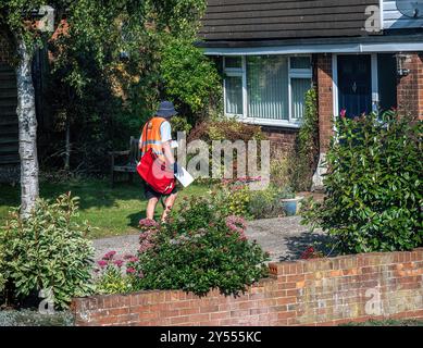 Facteur dans un uniforme rouge vif livrant des lettres à des maisons en Angleterre Banque D'Images