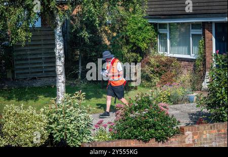 Facteur dans un uniforme rouge vif livrant des lettres à des maisons en Angleterre Banque D'Images