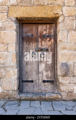 Une porte en bois vieilli avec quincaillerie en fer se tient fermement dans un mur de pierre en ruine, reflétant le charme d'un quartier historique. Les caractéristiques rustiques racontent une histoire de l'artisanat du vieux monde Banque D'Images