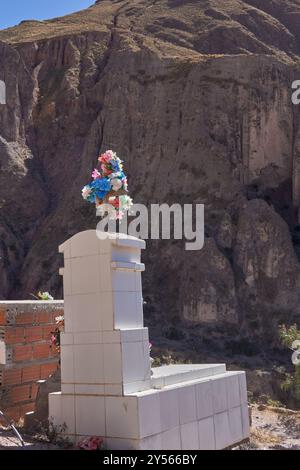 Pierre tombale blanche avec un bouquet de fleurs au milieu des montagnes à Iruya, Argentine. Banque D'Images