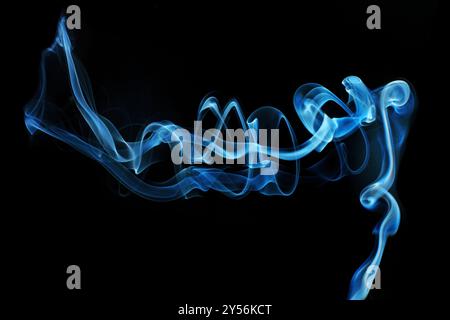 Fumée bleue de forme unique qui coule magnifiquement sur un fond noir créant une toile de fond abstraite. Banque D'Images
