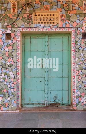 Tilora, Ajmer, Rajasthan, Inde. 9 novembre 2022. Porte turquoise dans un bâtiment décoré de carreaux cassés colorés. Banque D'Images