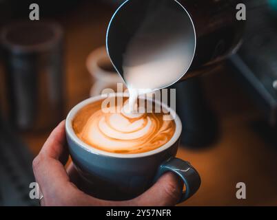 Un café versé dans une tasse bleue dans un café de Melbourne, en Australie. Le barista prépare du Latte art avec du lait cuit à la vapeur. Gros plan. Banque D'Images