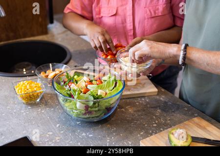 À la maison, la préparation de salade fraîche, deux amies féminines multiraciales ajoutant des ingrédients dans la cuisine Banque D'Images